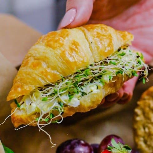 A hand holding a filled croissant sandwich
