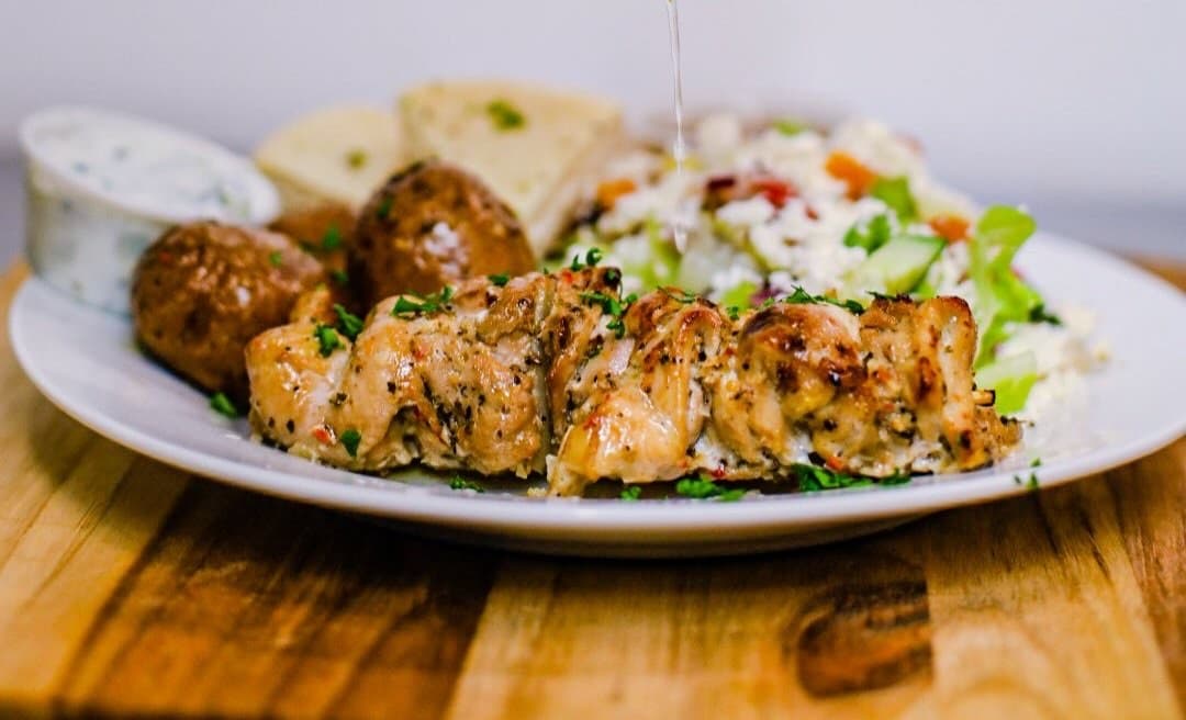 A plated grilled chicken dish with roasted potatoes and salad