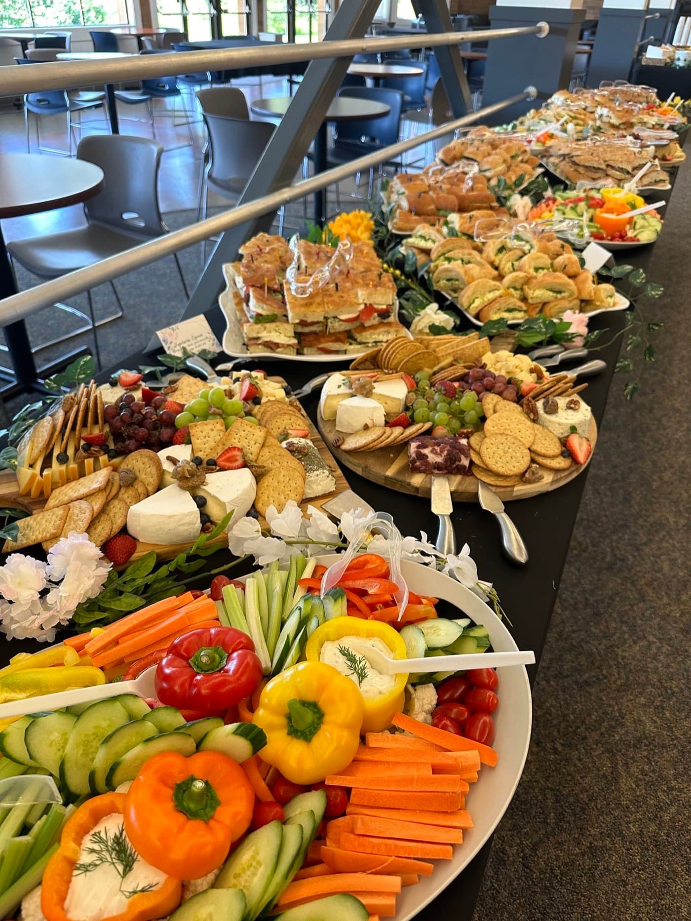 A buffet line of sandwich platters, a vegetable crudité platter, and a fruit platter set out for a reception